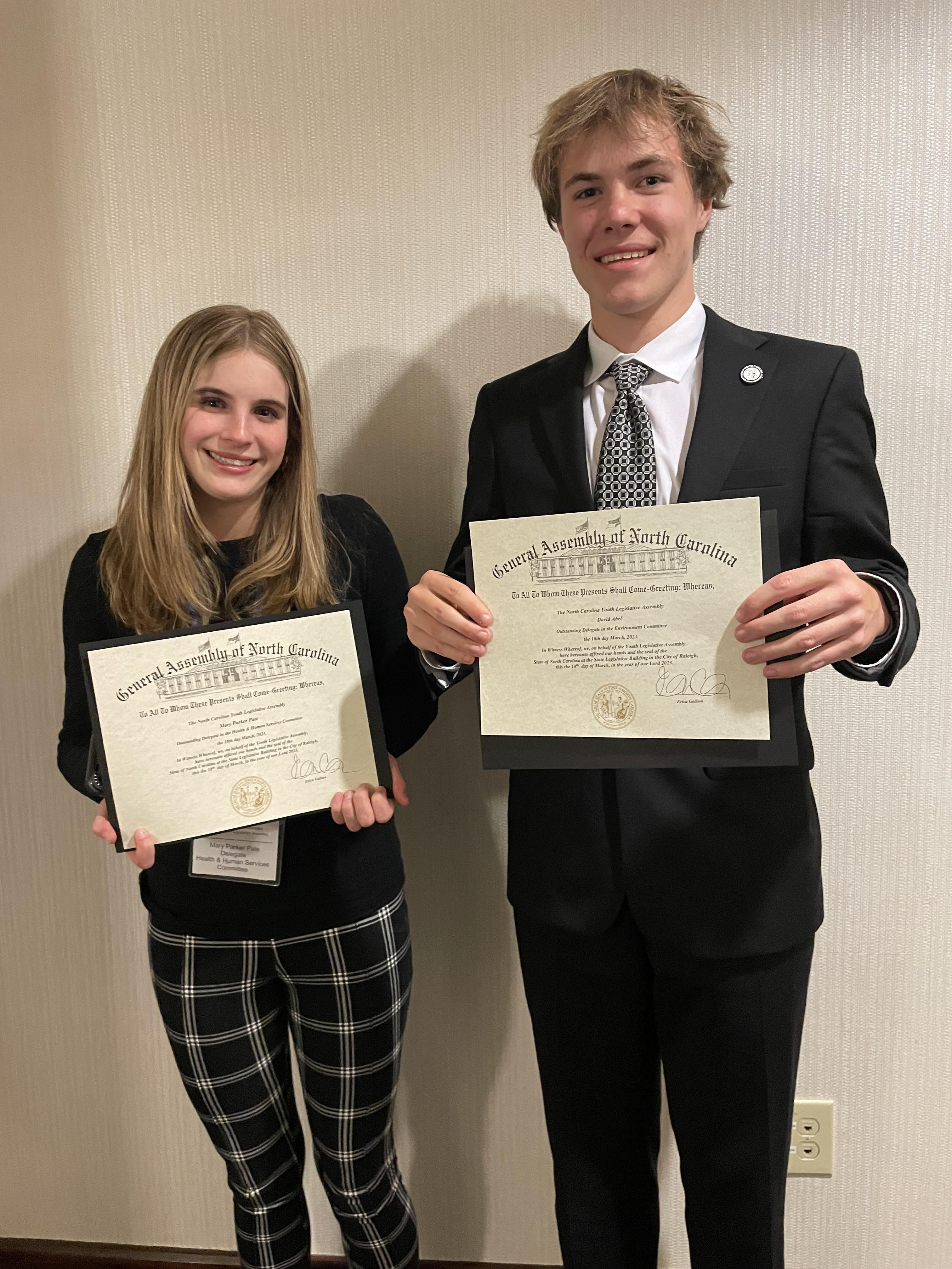two teens in professional clothing hold award certificates