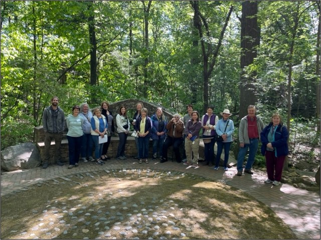 NC State Extension Master Gardener volunteers pose together on a path near trees and stone bench 